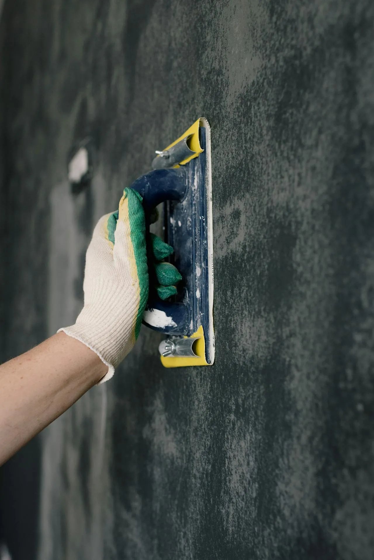 A trowel drawing a skim coat flat across a drywall surface